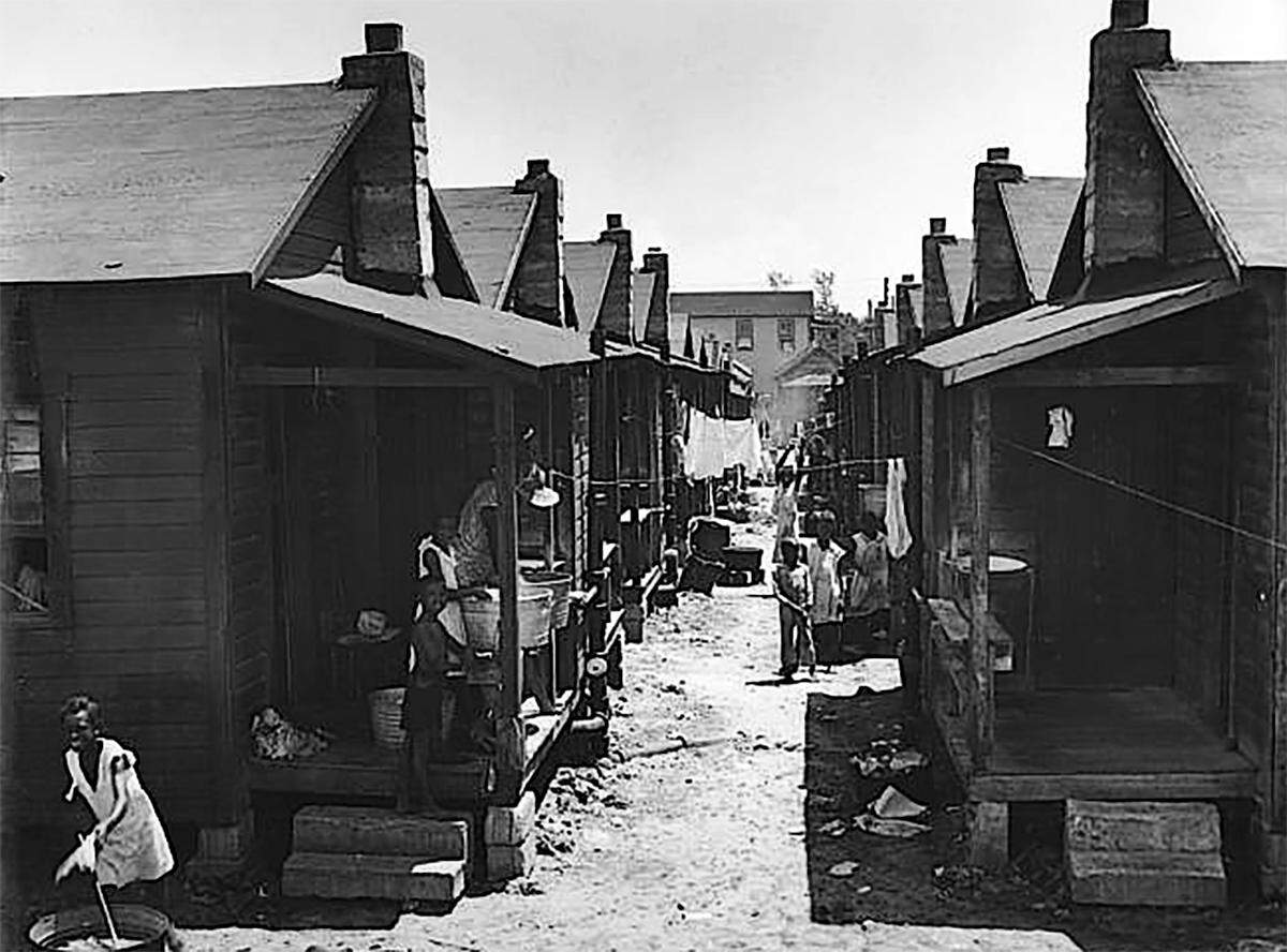 A photo of an unpaved back street in Overtown in the 1940s shows the crowded conditions and typical shotgun shack housing in the neighborhood.