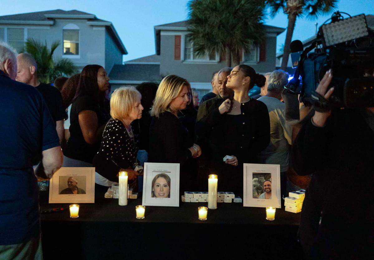 People walk past portraits of the victims of a triple homicide inside the Plum Bay community during a candlelight vigil on Sunday, Feb. 23, 2025, in Tamarac, Florida.