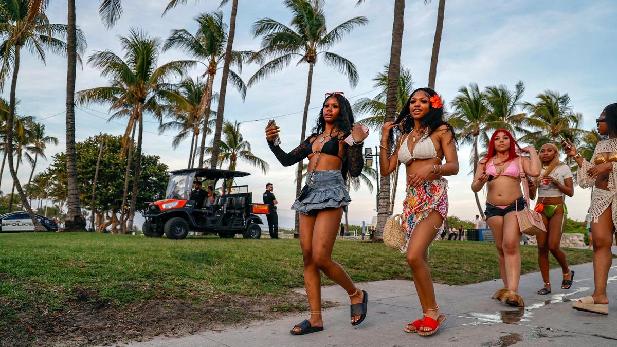 Spring breakers, who would only give their first name, Heaven, Brooklyn and Treasure, walk past Miami Beach police officers along Ocean Drive on Miami Beach, Florida on Friday, March 8, 2024.