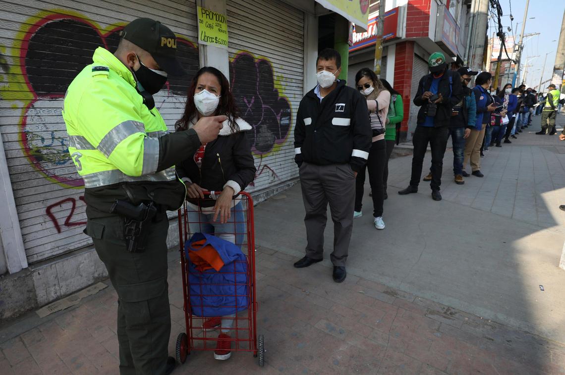 A police officer looks at a woman’s identification at a public bus station in Soacha on the outskirts of Bogotá, Colombia, Friday, March 27, 2020. Authorities have called for a complete lockdown of the country to help contain the spread of the new coronavirus, allowing residents to be outside their homes according to their ID numbers.