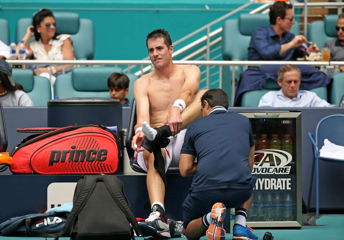 John Isner, of United States, is being treated by one coaching staff after injuring his foot during the final of the Miami Open tennis tournament against Roger Federer, of Switzerland, at Hard Rock Stadium on Sunday, March 31, 2019, in Miami Gardens, Fla. Roger Federer won 6-1, 6-4.
