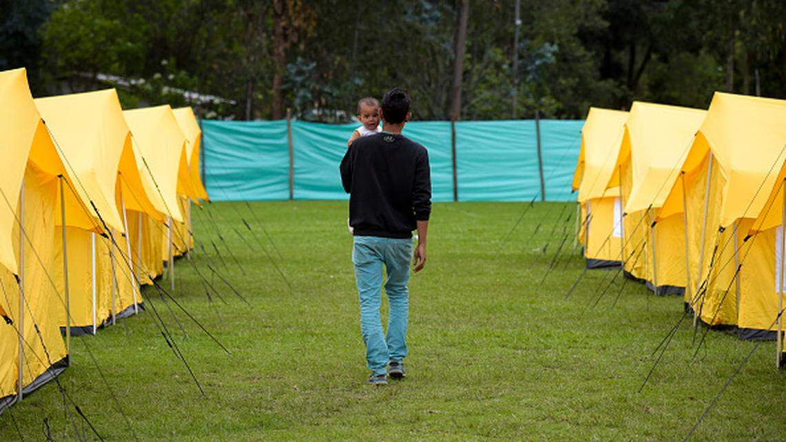 A Venezuelan refugee holding a small child walks inside a humanitarian camp in Bogota, Colombia, in 2018.