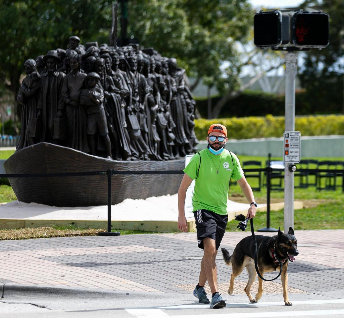 A pedestrian makes their way past the traveling bronze sculpture titled “Angels Unawares,” at Bayfront Park in downtown Miami on Wednesday, February 10, 2021. The life-sized sculpture will be open to the public daily for viewing until April 8. The sculpture weighs four tons and is 20-feet long. It features indigenous people, Jews fleeing Nazi Germany, Joseph, Mary, Jesus, and much more.