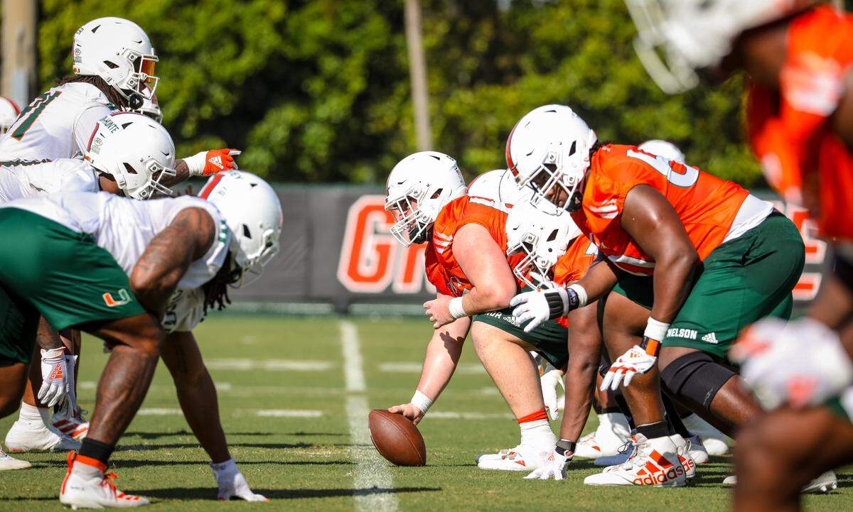The Miami Hurricanes offensive line, wearing orange jerseys, lines up against the defense during spring practice on March 16, 2021. Zion Nelson, UM’s left tackle, is in the foreground.