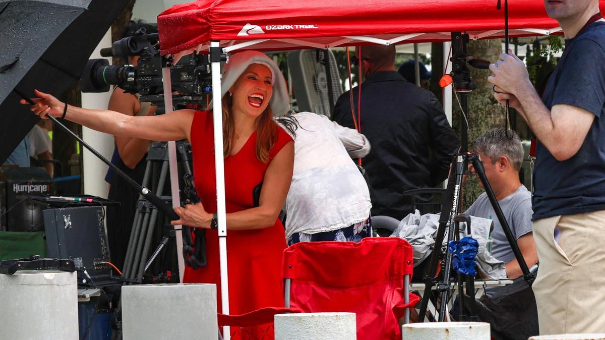 La periodista de Voice of America Celia Mendoza (izquierda) intenta cerrar su paraguas mientras cae la lluvia y los miembros de los medios de comunicación están cubriéndose del diluvio de la tarde. El lunes 12 de junio de 2023, miembros de los medios de comunicación se instalaban bajo la lluvia vespertina sobre el césped del Edificio de Tribunales Federales Wilkie D. Ferguson, Jr. en preparación de la comparecencia de Donald Trump este martes 13 de junio de 2023.