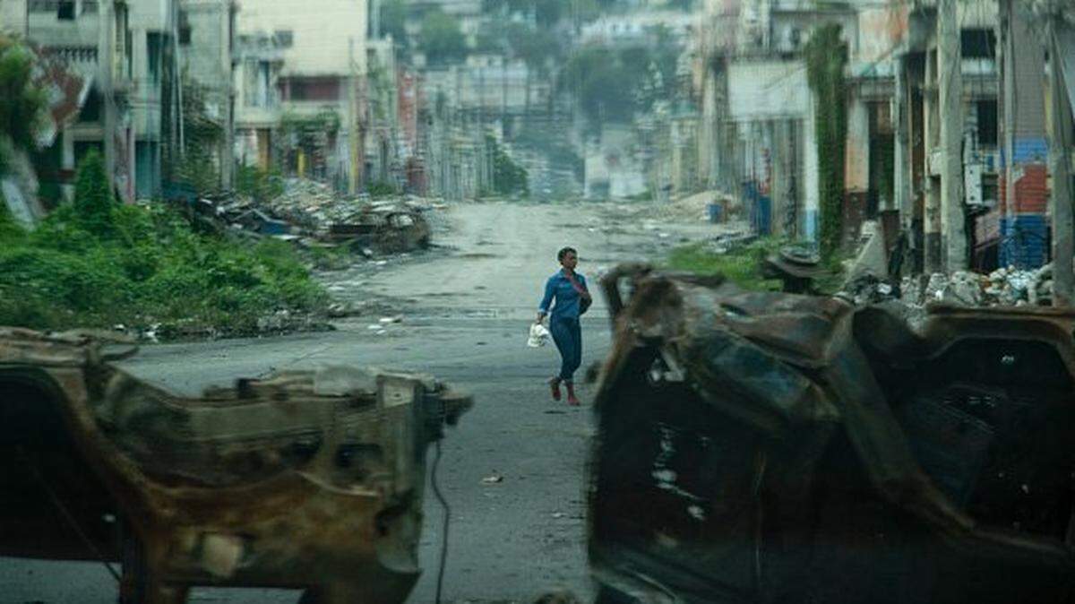 A walks past cars burned by armed gangs and used as a barricade during clashes last week with Haitian security forces on a deserted street in the city center, seen from an armored police vehicle during a patrol, in Port-au-Prince on January 16, 2026. An operation on January 14 by the Haitian National Police, conducted jointly with the army, the Gang Repression Force (FRG) and a mercenary unit, took place in the stronghold of Jimmy Chérizier, known as "Barbecue," leader of the "Viv Ansanm" gang, in one of his residences in the Delmas 6 district, 6km (4 miles) west of downtown Port-au-Prince, although he was absent at the time of the operation. (Photo by Clarens SIFFROY / AFP via Getty Images)