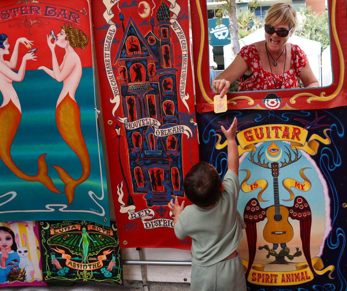 Maximo Bray, 2, reaches for tarot card from artist Molly McGuire as he and his family stop by to look in her booth at the Coconut Grove Art Festival. 