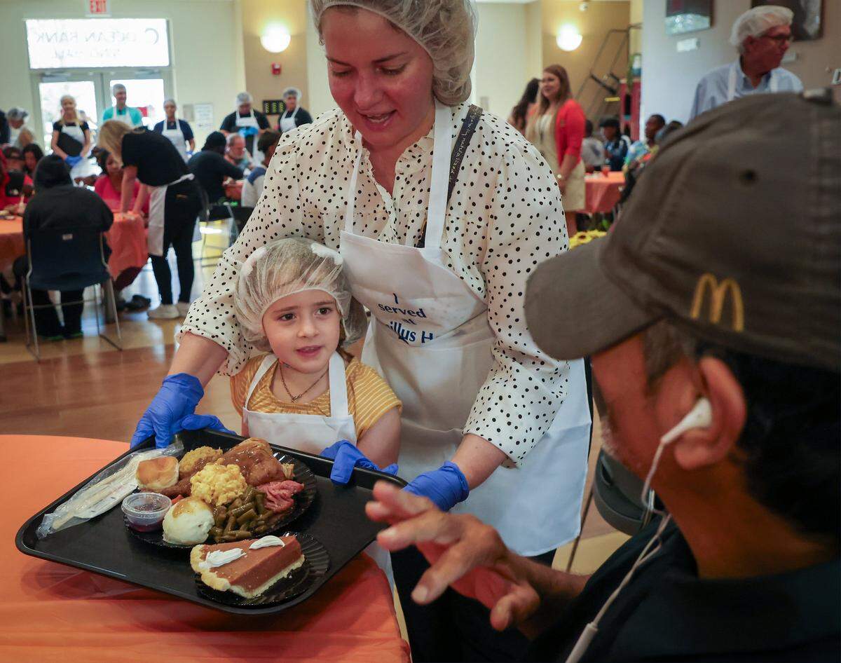 Volunteers Anastasia Fernandez, 6, left, gets help from her mother Carolina Vester, 40, as she delivers a meal.  Camillus House held its 65th annual Thanksgiving Celebration, a cherished tradition that brings hope, dignity, and fellowship to hundreds of individuals experiencing shelter insecurity with a Thanksgiving dinner and other activities at its main campus on Thursday, November 27, 2025, in Miami, Florida. 