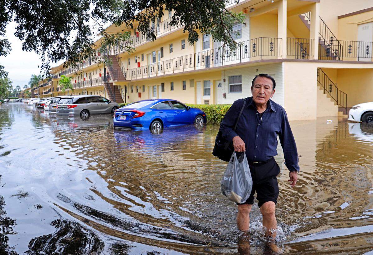 Homero Giviria, 76, walks to his job at Aventura Mall barefooted with his dry shoes in a plastic bag through Biscayne Lake Gardens apartment complex in Aventura, Florida, on Monday, December 23, 2019.