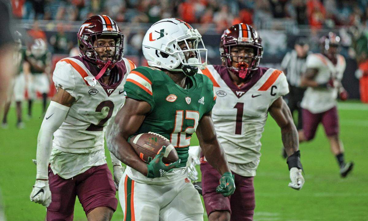 Miami Hurricanes wide receiver Brashard Smith (12) runs to score on a pass reception from quarterback Tyler Van Dyke (9) in the second quarter as Virginia Tech Hokies defensive back Jermaine Waller (2) and defensive back Chamarri Conner (1) give chase at Hard Rock Stadium in Miami Gardens on Saturday, November 20, 2021
