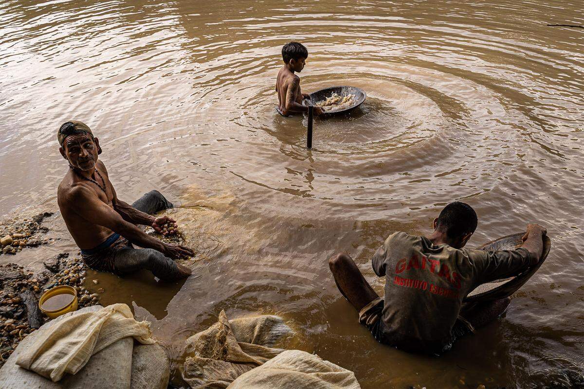 Dos hombres y un niño buscan oro en un río cerca de la mina Las Parcelas en Tumeremo, Venezuela. El uso del mercurio en el proceso ha contaminado muchos ríos como este. Y el atractivo del dinero que se puede ganar en la minería ilegal de oro ha convertido a algunos niños abandonen la escuela para tratar de ganar algún dinero.