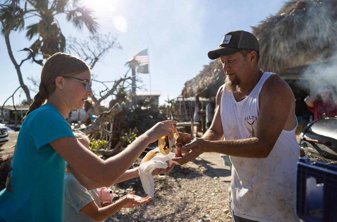 Johnny Smith, 49, the owner of Low Key Tiki, gives Cay Stevens, 13, and Marina Stevens, 6, food outside of his restaurant on Friday, Sept. 30, 2022, in St. James City, Florida. The local American Legion post donated their food for a community cookout. Hurricane Ian made landfall on the coast of Southwest Florida as a Category 4 storm Wednesday afternoon, leaving areas affected with flooded streets, downed trees and scattered debris.
