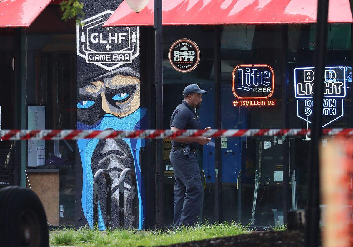 An officer with the Jacksonville Sheriff’s Office walks past the GLHF Game Bar, where 3 people, including the gunman, were killed at the Jacksonville Landing on Sunday in Jacksonville, Florida.
