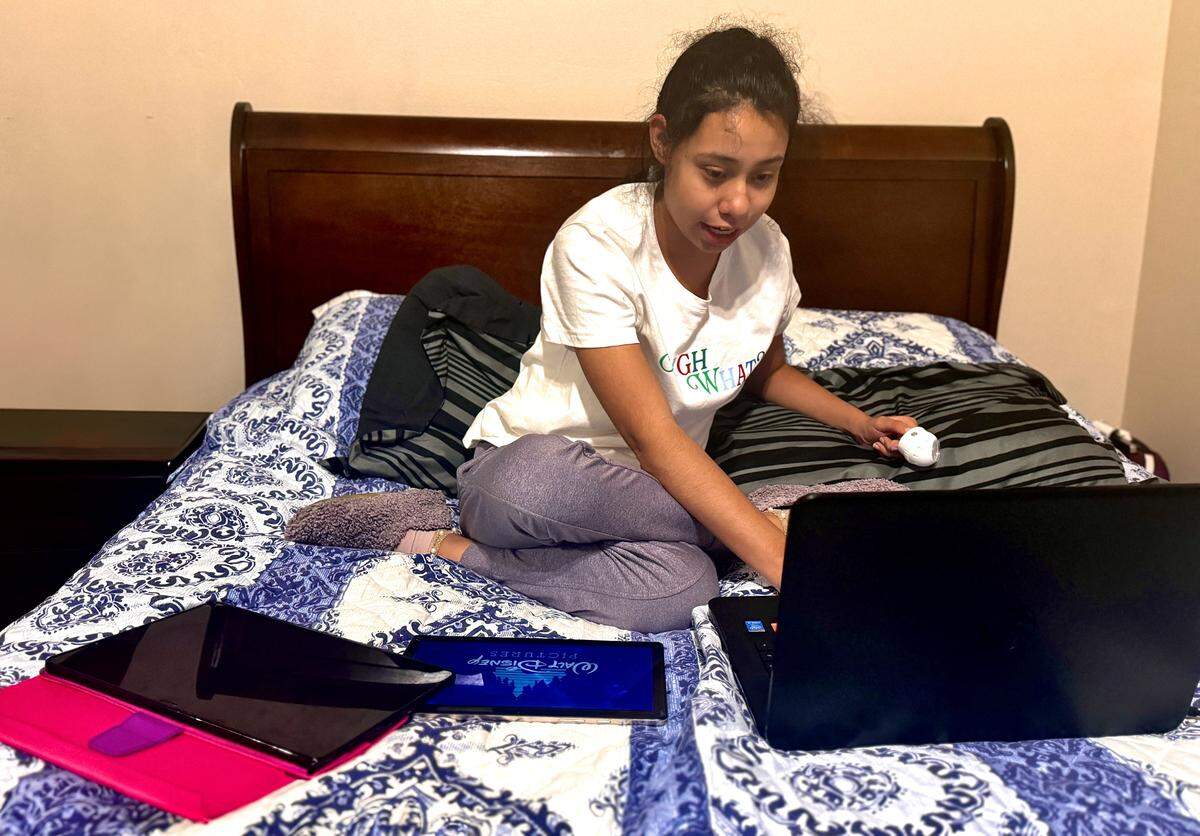 Michaela Aguilar using her computer along with two tablets in her bedroom in Kendall.