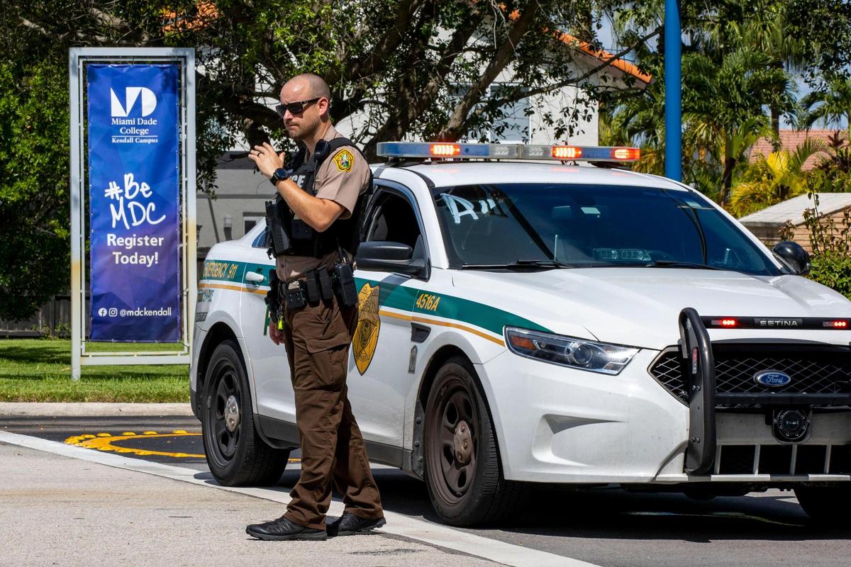 A Miami-Dade Police officer waves motorists past the Southwest entrance to Miami-Dade College Kendall Campus as a part of a lockdown protocol in response to a suspicious bicyclist near campus, in Miami, Florida, on Wednesday, August 17, 2022.
