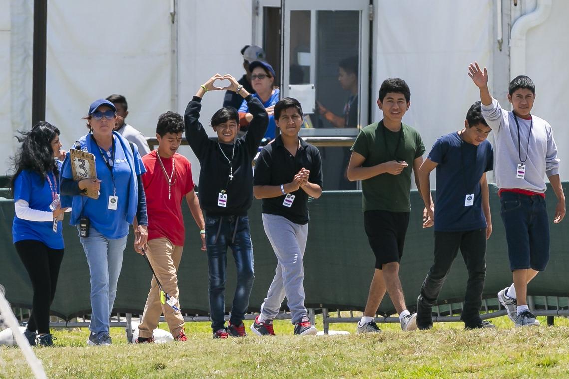 Migrant children wave at protestors while being escorted throughout the Homestead Temporary Shelter for Unaccompanied Children during Good Friday in Homestead, Florida on April 19, 2019.