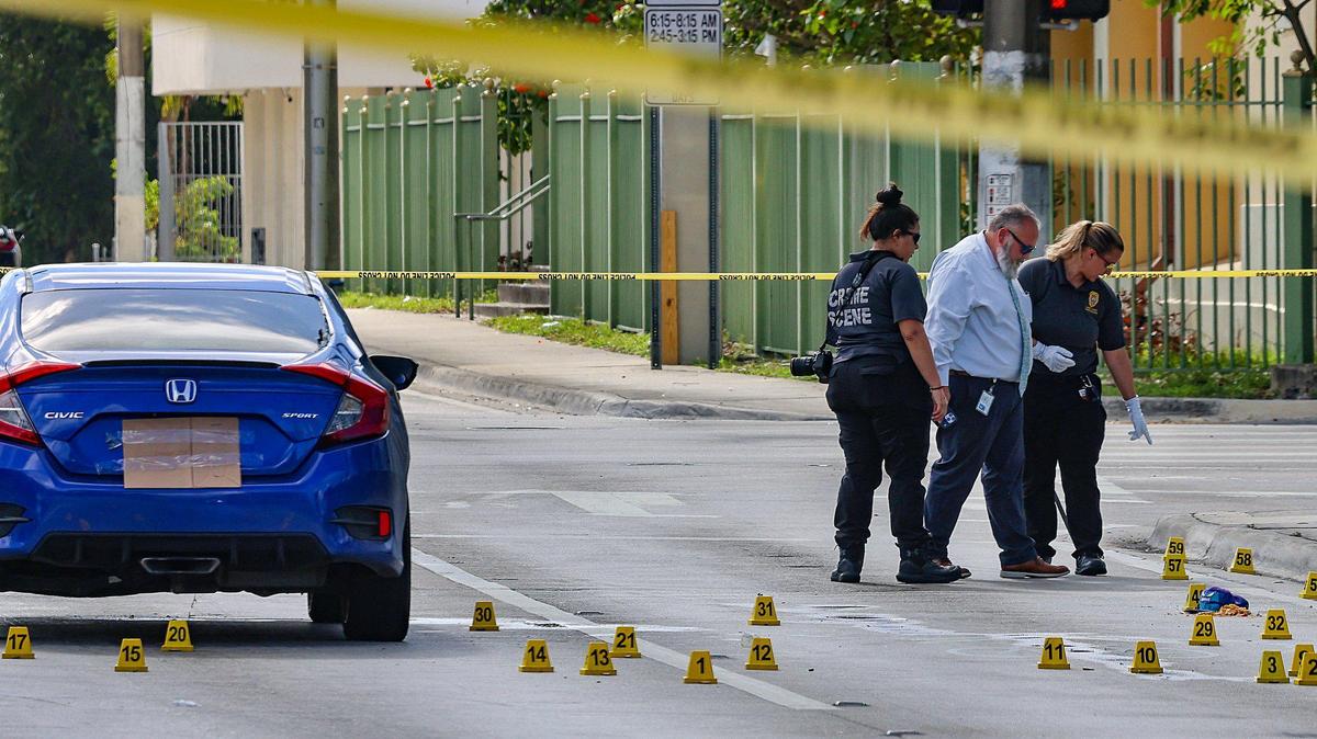 Miami police and crime scene investigators look downward onto a road littered with gun casings. Investigators probe the area where four people were shot, two of them killed, after an early morning shooting just east of I-95 near the intersection of Northwest 62nd Street and Northwest Second Avenue in Miami on Monday, June 16, 2025.