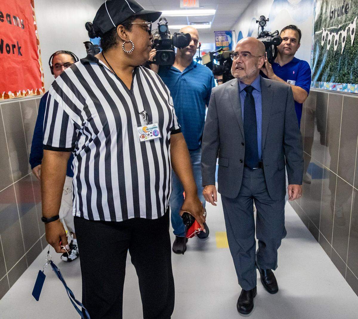 La Dra. Orna Campbell, a la izquierda, lleva al superintendente escolar de Miami-Dade, José Dotres, a hacer un rápido recorrido por algunas aulas de la escuela primaria Comstock, en 2420 NW 18 Ave. el miércoles en Allapatah. La Dra. Campbell, directora de la escuela, se vistió de árbitro porque ahora que el año escolar ha comenzado, está de vuelta en el juego.