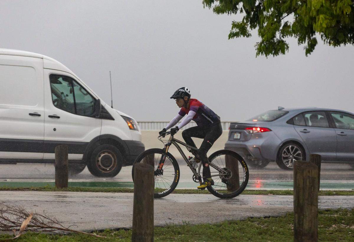 A cyclist makes his way toward the William M. Powell bridge along the Rickenbacker Causeway as lightning and heavy rain falls in the area on Monday, June 19, 2023, in Miami, Fla.