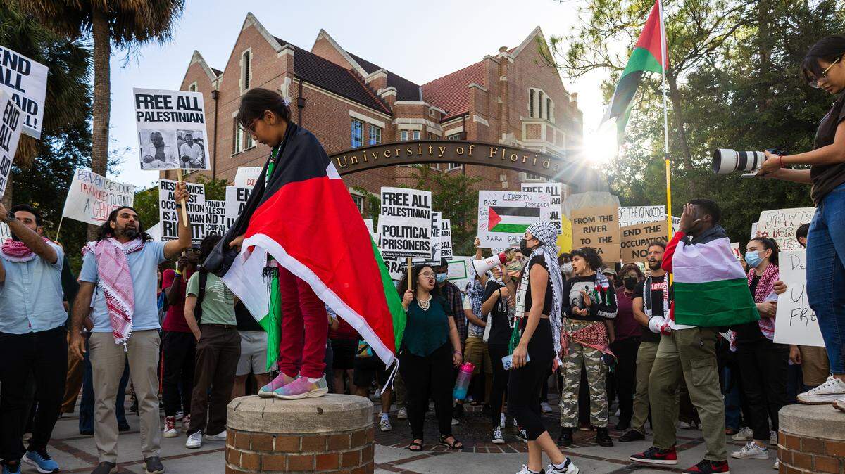 A girl wrapped in a Palestinian flag stands on a bollard as protestors advocating for the end of the siege on Gaza gather on the corner of University Avenue and 13th Street at the University of Florida in Gainesville on Oct. 25, 2023.