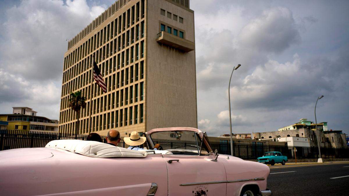 Tourists take a joy ride in a vintage convertible car as they pass the U.S. embassy in Havana, Cuba.