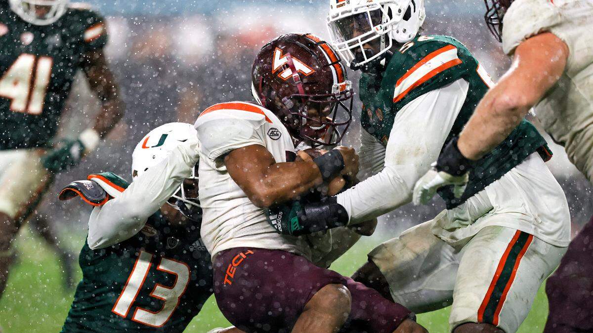 Miami Hurricanes defensive end Deandre Johnson (13) and defensive lineman Leonard Taylor (56) bring down Virginia Tech Hokies running back Raheem Blackshear (5) during the fourth quarter of their ACC football game at Hard Rock Stadium on Saturday, November 20, 2021 in Miami Gardens, Florida.