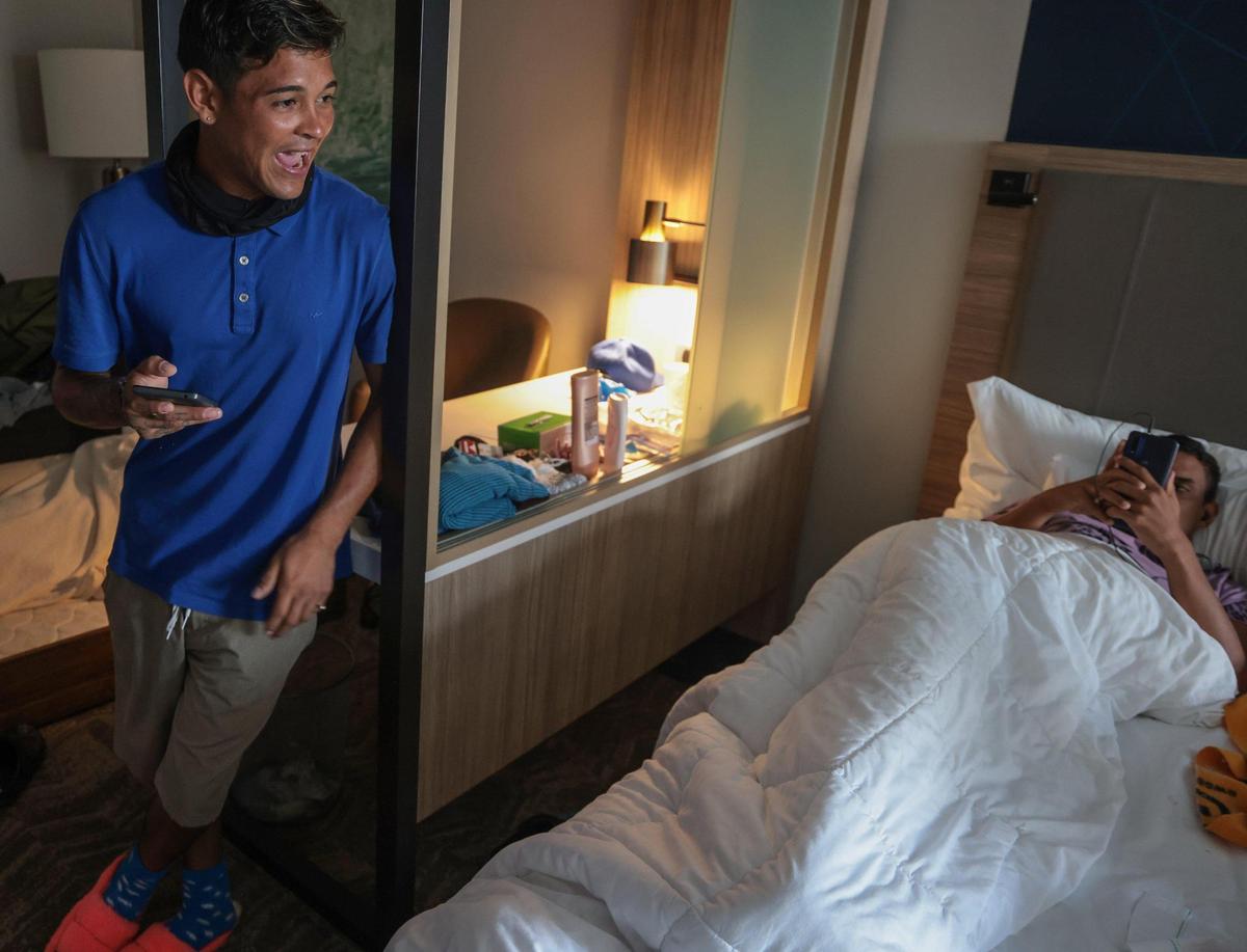 Pedro Escalona, 24, left, chats with his fellow migrants in a hotel room provided by their former employer.