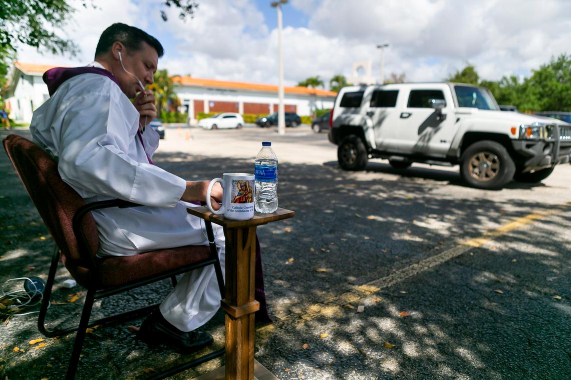 Father Richard Vigoa, the administrator of St. Augustine Church, talks with a churchgoer for a drive-thru confession in Coral Gables, Florida on Saturday, March 21, 2020. Due to COVID-19, churches have had to use technology and different ideas to help reach their parishioners.
