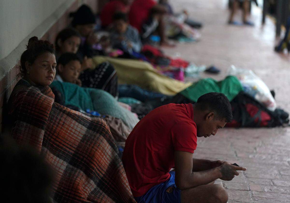 Venezuelan migrants sit along a building wall as they take cover from the rain, near the banks of the Rio Grande in Matamoros, Mexico, Saturday, May 13, 2023.