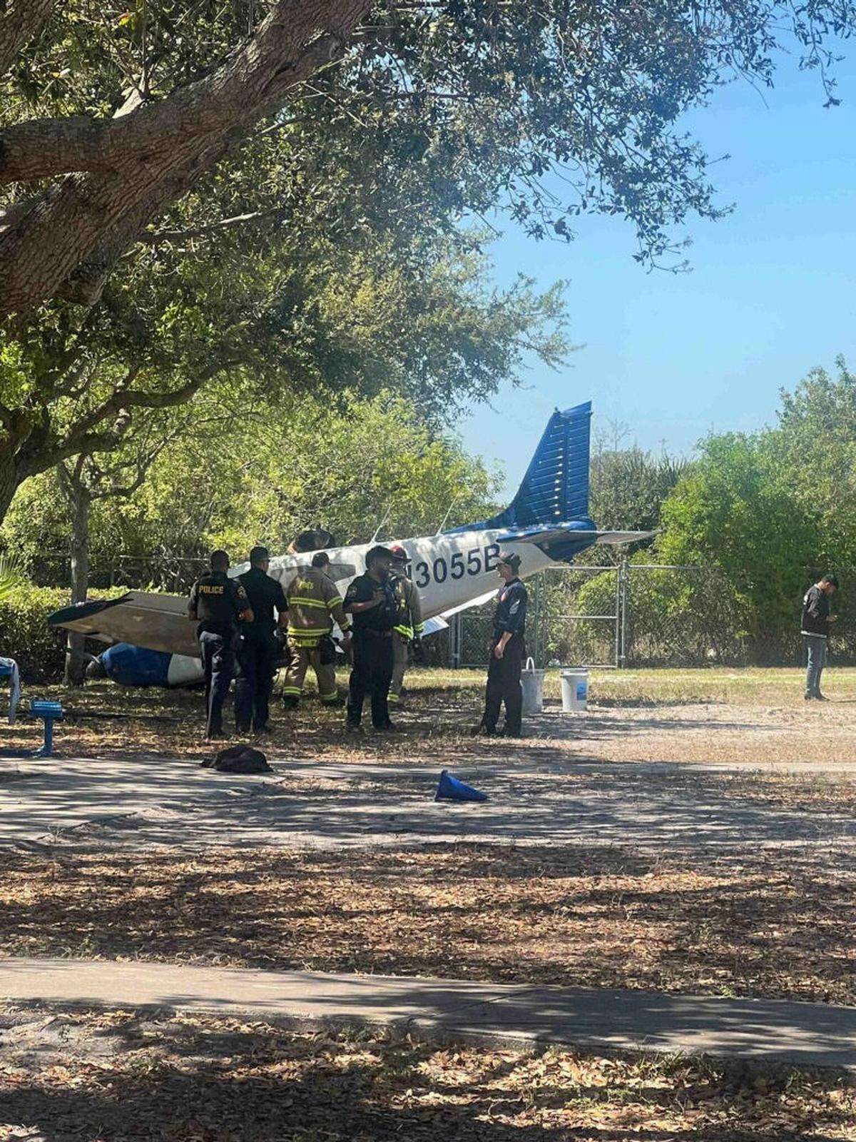 Police officers and firefighters gather near a single-engine Piper airplane sitting with its nose on the ground in a field at Coconut Palm Elementary School in Miramar, Florida, Wednesday, March 12, 2025.