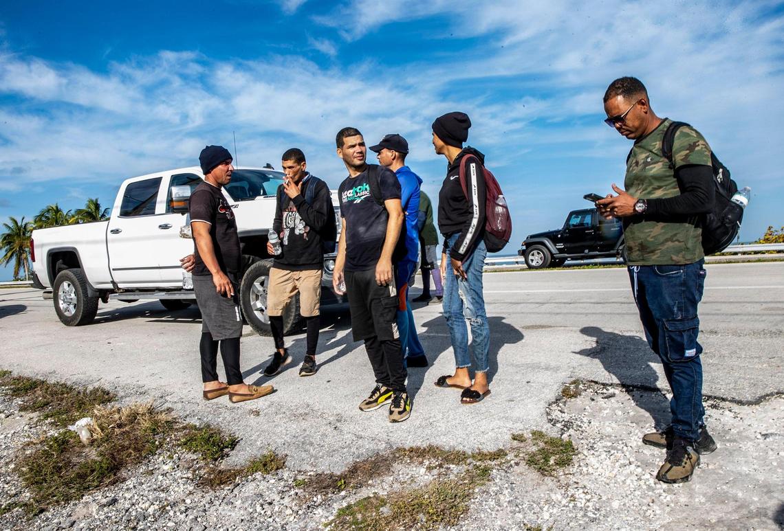 Members of two groups of Cuban migrants from Matanzas — one with 19 people, the other with 12 — stand in the sun on the side of U.S. 1 in the Middle Keys island of Duck Key on Monday, Jan. 2, 2023. By noon, they said they had been standing there waiting to be picked up by U.S. Border Patrol agents since arriving in two rustic vessels at 2:30 a.m.