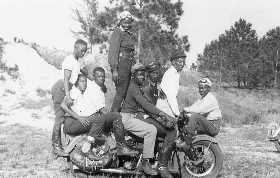 Bessie Stringfield, known as the “Motorcycle Queen of Miami,” stands atop a motorcycle flanked by young male couriers in the 1940s. Stringfield is the subject of a documentary film, “To Myself With Love: The Bessie Stringfield Story.”