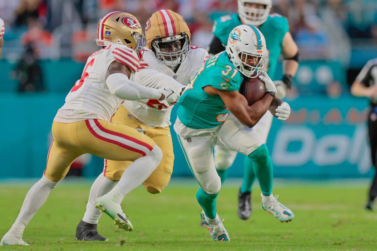 Miami Dolphins running back Raheem Mostert (31) carries the ball as San Francisco 49ers safety Malik Mustapha (6) and defensive tackle Evan Anderson (69) defend during the first half of an NFL Football game at Hard Rock Stadium in Miami Gardens, Florida, on Sunday, December 22, 2024.
