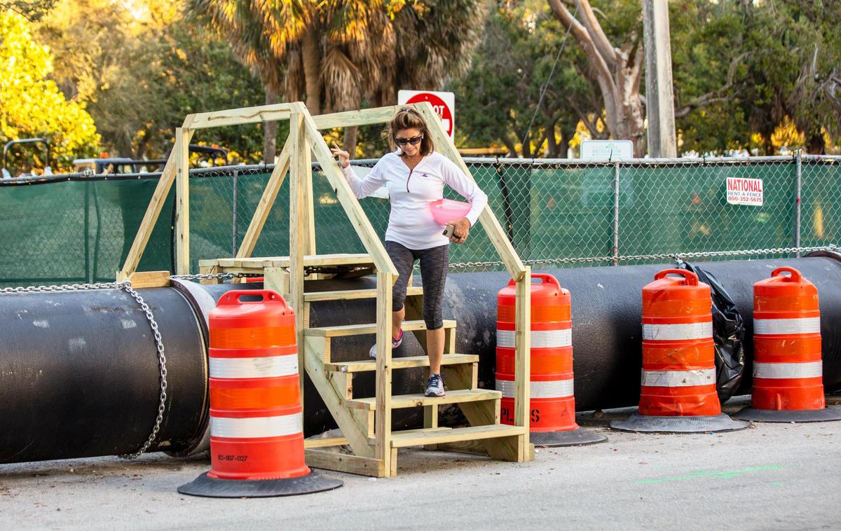 Tracey Bartholomew, a Rio Vista neighborhood resident for 35 years, climbs down an improvised ‘bridge’ constructed to let residents cross a temporary above-ground sewage pipe, in Fort Lauderdale, Florida, on Tuesday, January 7, 2020.
