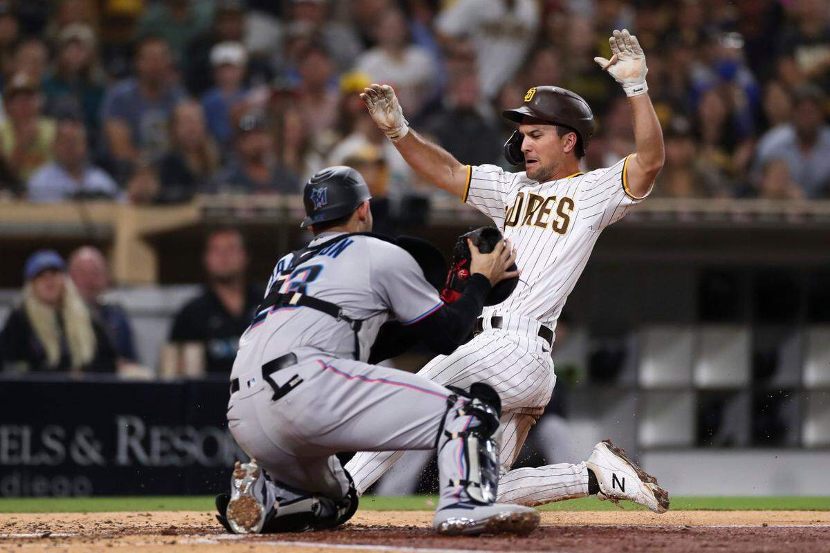 San Diego Padres’ Adam Frazier, right, is tagged out by Miami Marlins catcher Alex Jackson as he attempts to score on a sacrifice fly hit by Jake Cronenworth in the third inning of a baseball game Monday, Aug. 9, 2021, in San Diego.