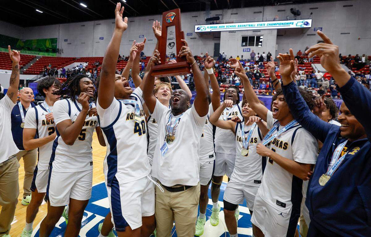St. Thomas Aquinas Raiders head coach Julius Sandi raises the championship trophy as the team celebrates the win over Evans for the FHSAA Class 6A Boys High School Basketball State Championship.