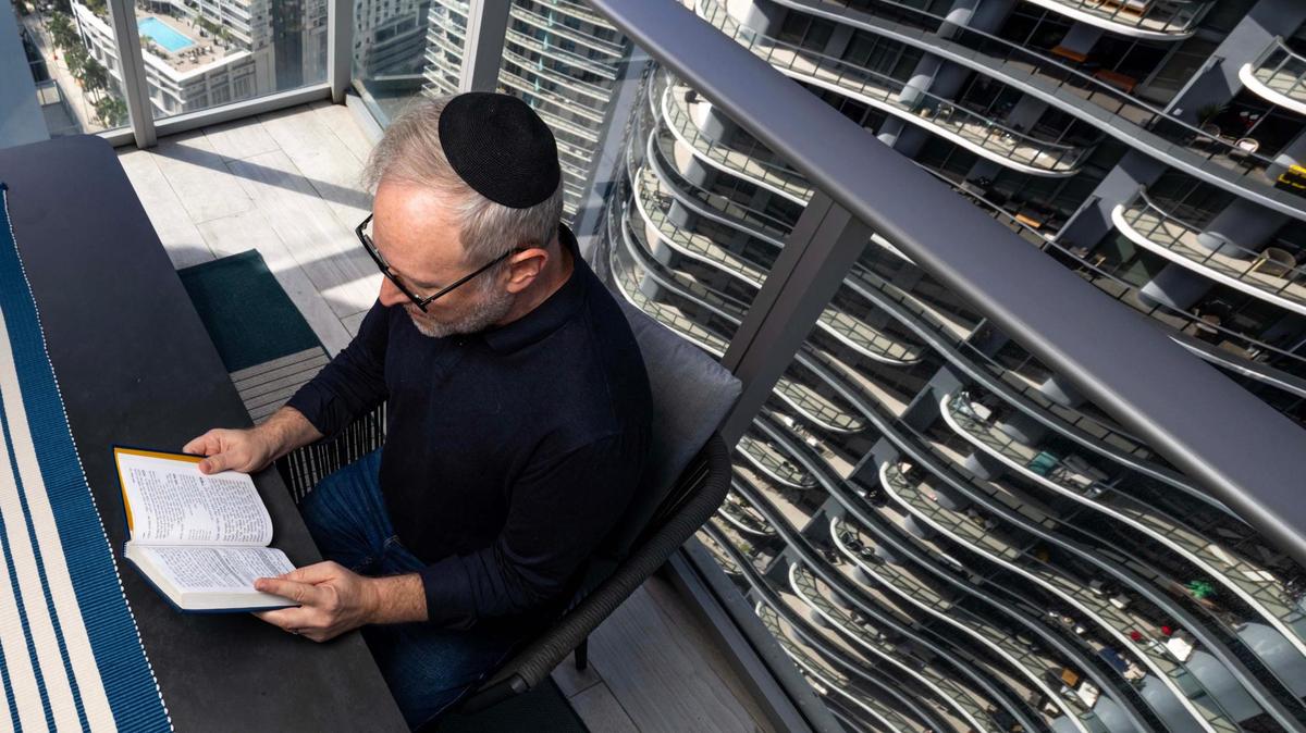 Daniel Gammerman sits on his apartment balcony overlooking the Brickell neighborhood as he reads from his prayer book. Gammerman has struggled to find an Orthodox synagogue that will accept him as an openly gay man.