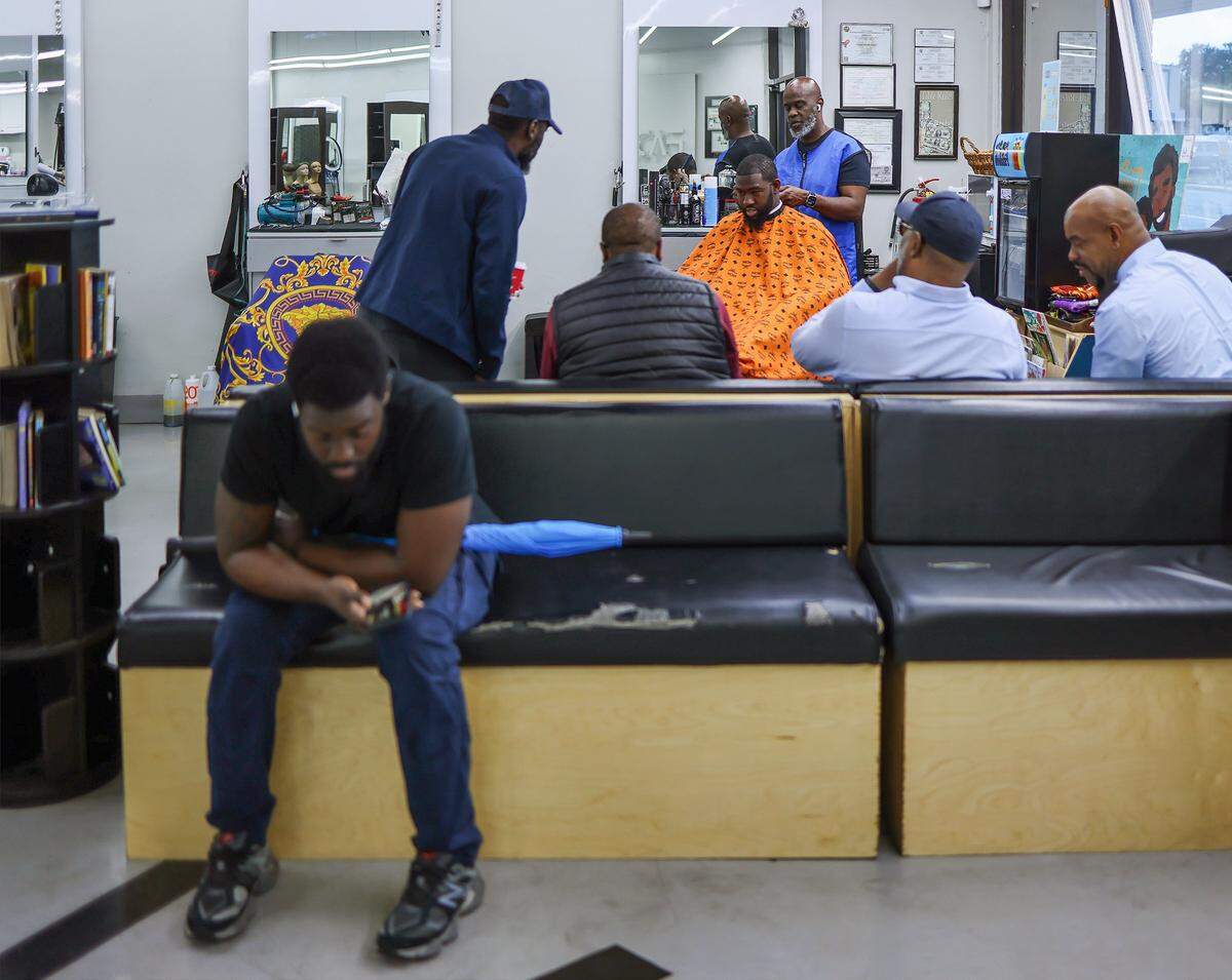 Barbershop owner Michael Stephens, 58, cuts the hair of Jefferson Noel, 31, founder of “Barbershop Speaks,” as several customers and conversation participants gather at Topcuttaz on Wednesday, October 29, 2025, in Miami Gardens, Florida. Six Black men - educators, community advocates, activists, and entrepreneurs gathered at the Topcuttaz barbershop to talk shop about the conditions of Black people in South Florida, a year after the election, and the impact of the first nine months of Trump’s administration.