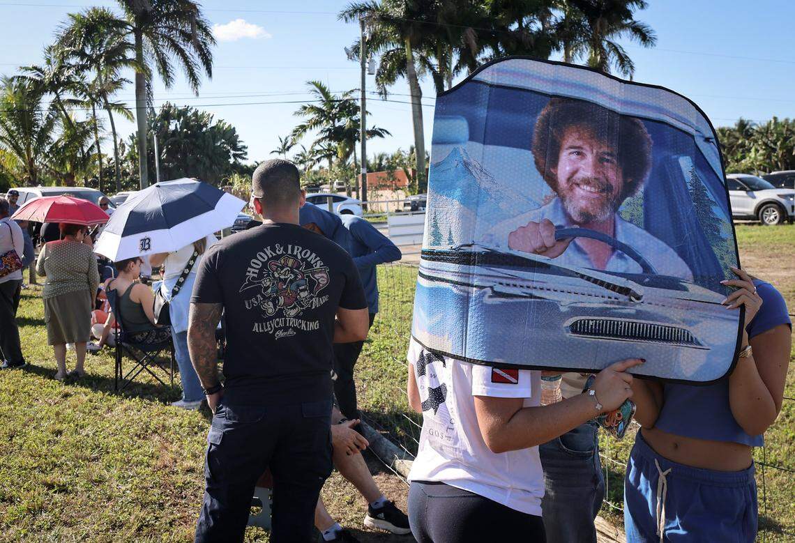Sofia Periera, 18, left, Victoria Acosta, 21, and Ashley Marmol, 19, right, shield themselves from the sun with a Bob Ross car visor while waiting in line for more than two hours to place their cinnamon rolls order. Knaus Berry Farm opened at its new location, offering shakes, baked goods, and the cinnamon rolls for which it became famous. At the same time, some customers wanted shakes, most lined up for cinnamon rolls, and some even arrived the night before to ensure success on Monday, December 22, 2025, in Redlands, near Homestead, Florida.