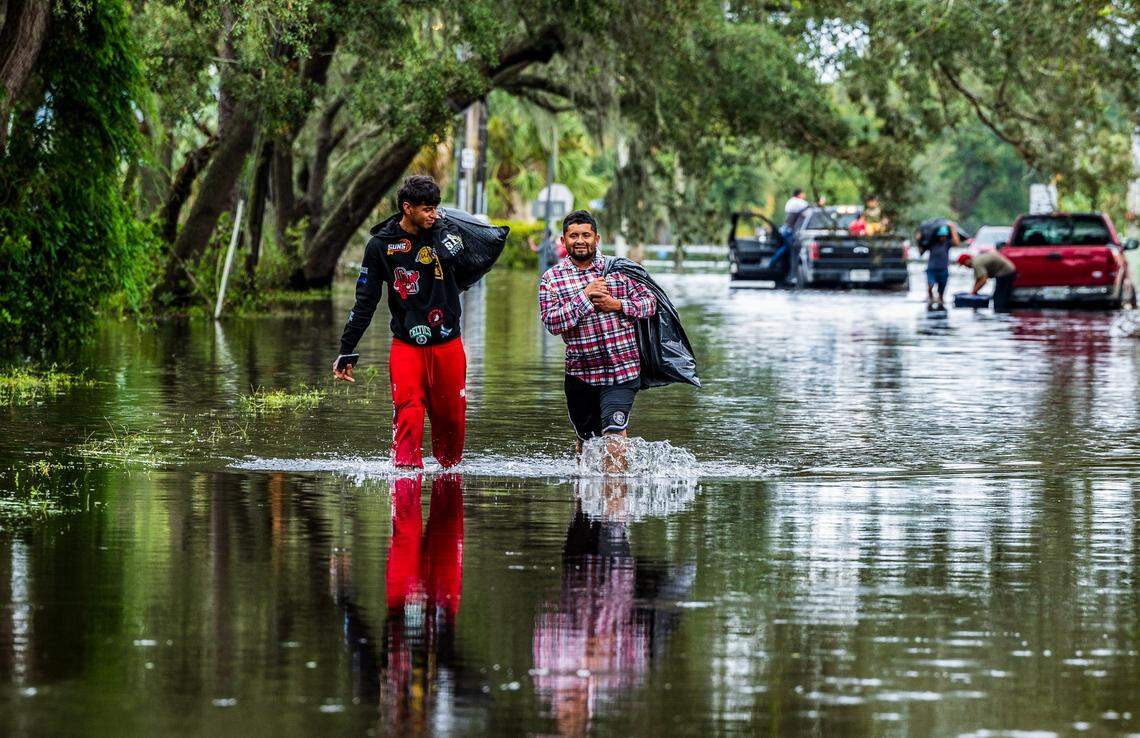 Juan Jose Muñoz (left) and Elvin Antonio Urbina walk with her belongings through the flooded N 15th St in North Tampa, Thursday, October 10, 2024, a day after Hurricane Milton crossed Florida’s Gulf Coast.
