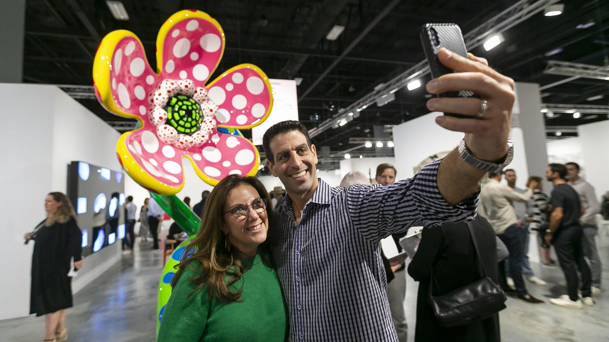 Michele Scheck and her husband, Steven Scheck, take a selfie next to “Flowers that speak all about my heart given to the sky” by Yayoi Kusama during Art Basel at the Miami Beach Convention Center in December.