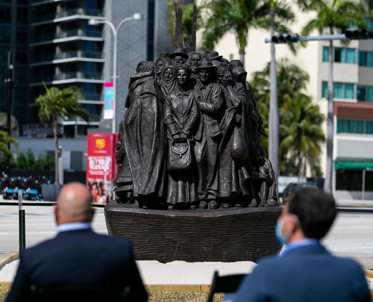 People listen as Archbishop Thomas Wenski speaks next to a sculpture titled “Angels Unawares,” at Bayfront Park in downtown Miami on Wednesday, February 10, 2021. The traveling bronze, life-sized sculpture will be open to the public daily for viewing until April 8. The sculpture weighs four tons and is 20-feet long. It features indigenous people, Jews fleeing Nazi Germany, Joseph, Mary, Jesus, and much more.