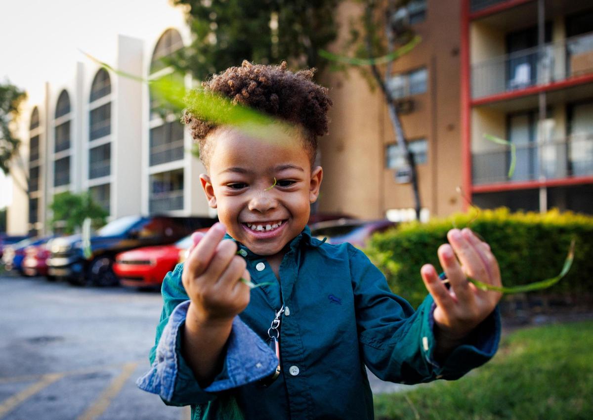 Ryan Hiott Jr. plays while throwing grass in the air outside of the apartment building where his family lives on Wednesday, Oct. 23, 2024, in Miami.
