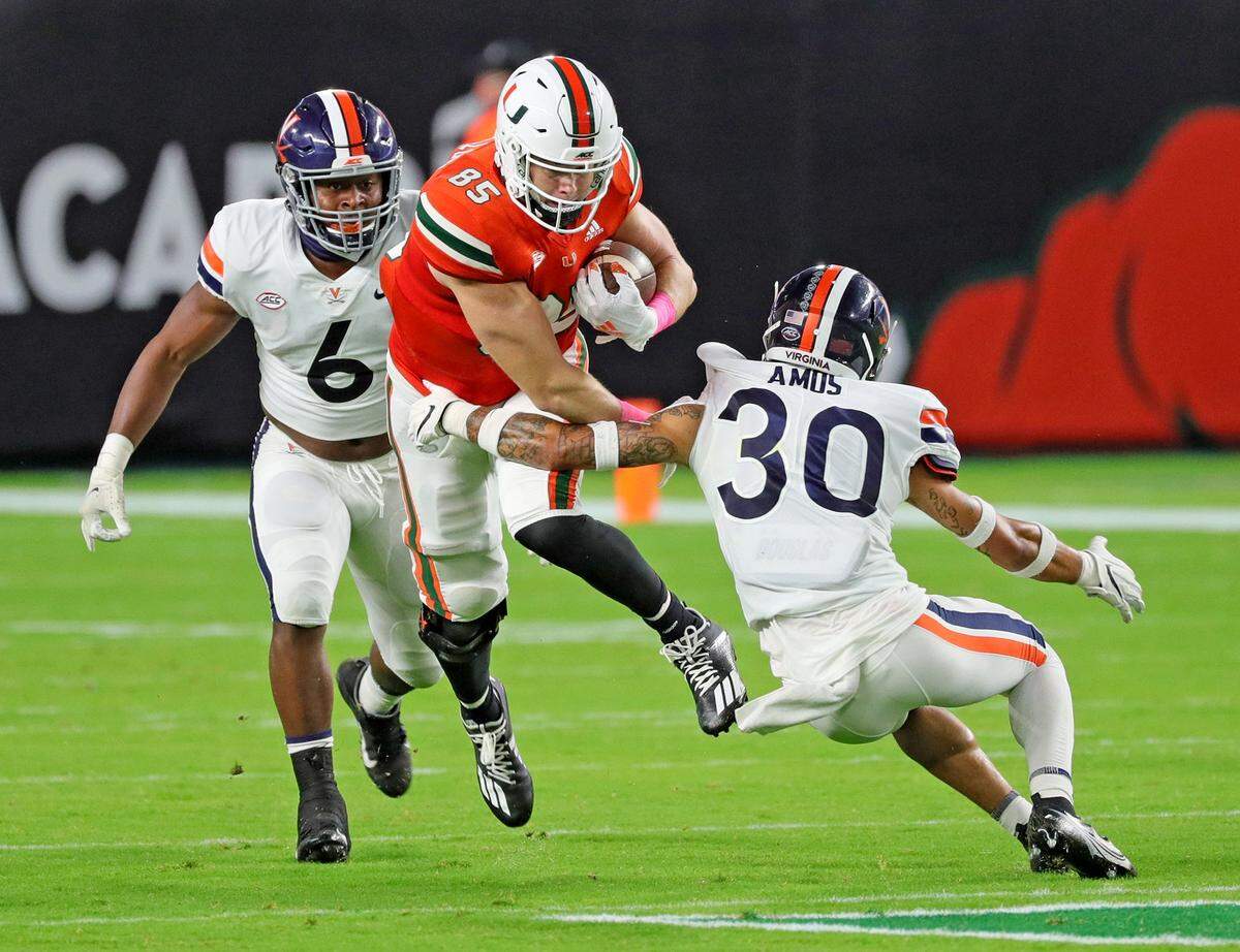 Miami Hurricanes tight end Will Mallory (85) runs the ball as Virginia Cavaliers Nick Jackson (6) and D’Angelo Amos (30) defend in the first quarter at Hard Rock Stadium in Miami Gardens, Florida, Saturday, October 24, 2020.
