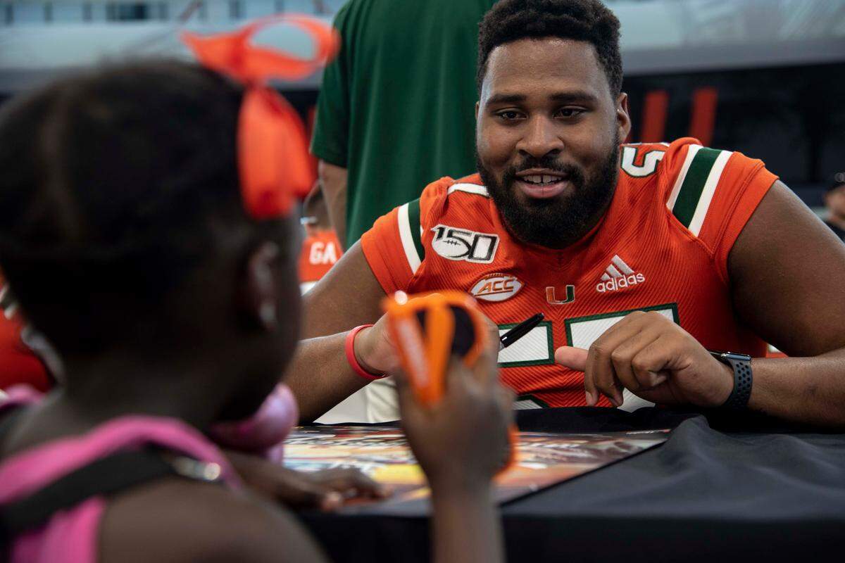 Kai-Leon Herbert (57) signs a poster for Haddasha Herring, 3, during CanesFest at University of Miami on August 3, 2019.