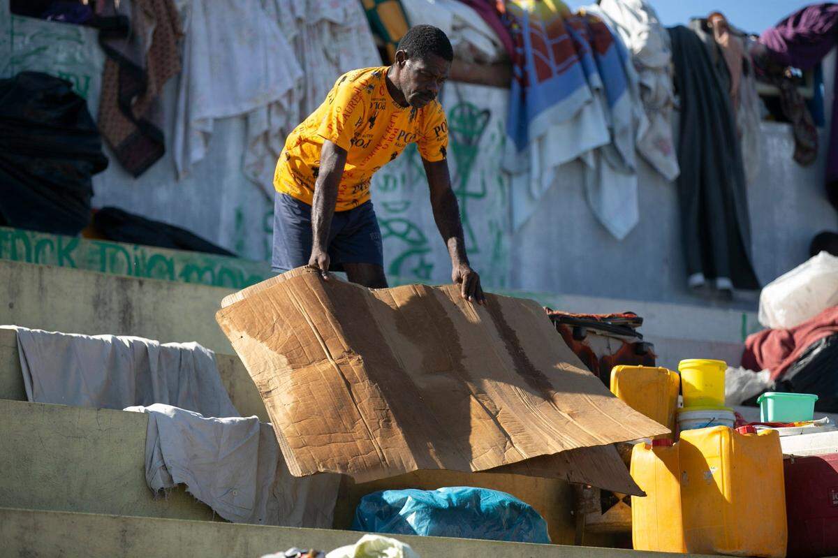 Un hombre seca un trozo de cartón que usa para dormir en la plaza pública Hugo Chávez transformada en un refugio para las familias que se ven obligadas a abandonar sus hogares debido a los enfrentamientos entre pandillas armadas en Puerto Príncipe, Haití, el jueves 20 de octubre de 2022.