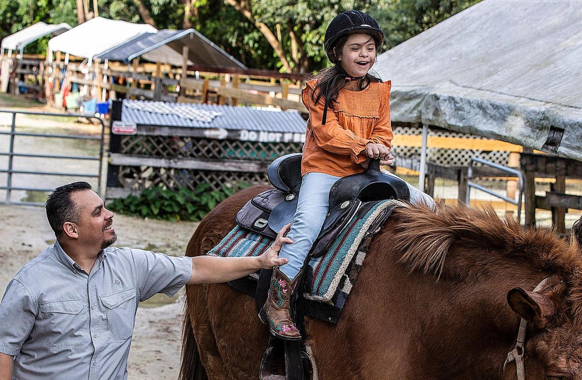 Ronnie López sostiene a su hija Angelina López mientras monta a Sampson, un caballo de la HAPPI Farm. "La primera vez que montó supimos enseguida que este era su lugar feliz", dijo su madre, Glenda López.