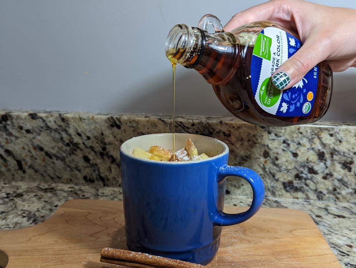 Maple syrup is being poured into French toast in a blue mug.