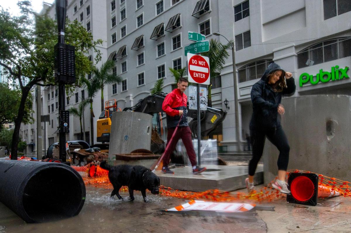 A man and a woman walk their dog on a submerged sidewalk due to flooding on Southwest First Avenue in the Brickell neighborhood of Miami, Florida, on Saturday, June 4, 2022. Publix closed its store there temporarily due to the rains.