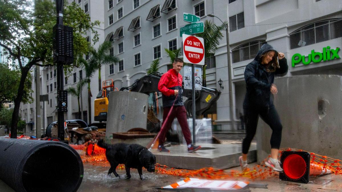 A man and a woman walk their dog on a submerged sidewalk due to flooding on Southwest First Avenue in the Brickell neighborhood of Miami, Florida, on Saturday, June 4, 2022.